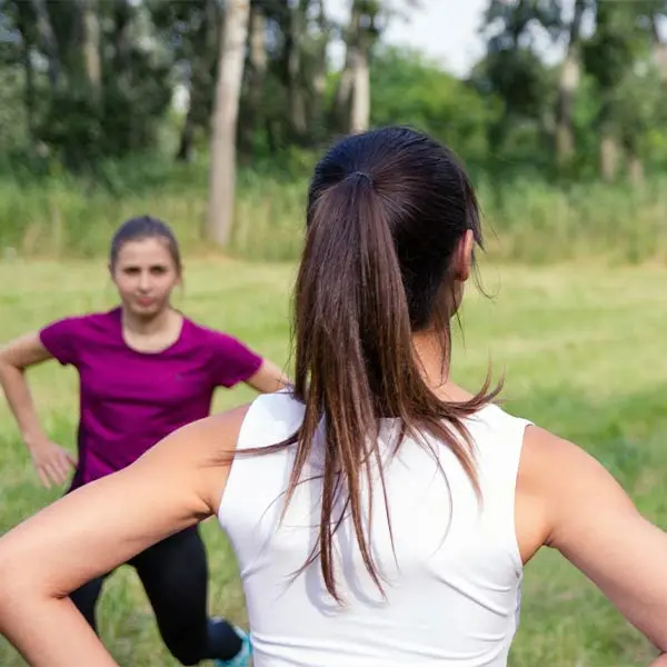 Insegnante di pilates di spalle che tiene una lezione di pilates all'aperto davanti a un'altra ragazza che la emula.