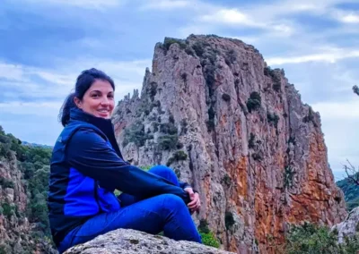 Veronica Murgia di Vemu Inclusive Hikes sorridente seduta su una roccia, con una maestosa parete rocciosa sullo sfondo