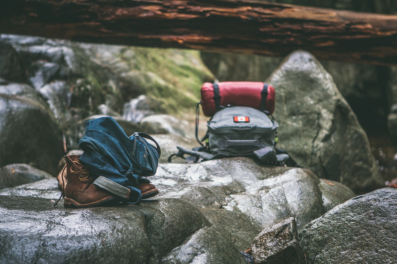 zaino da trekking posato su delle rocce grigie sotto un tronco d'albero caduto